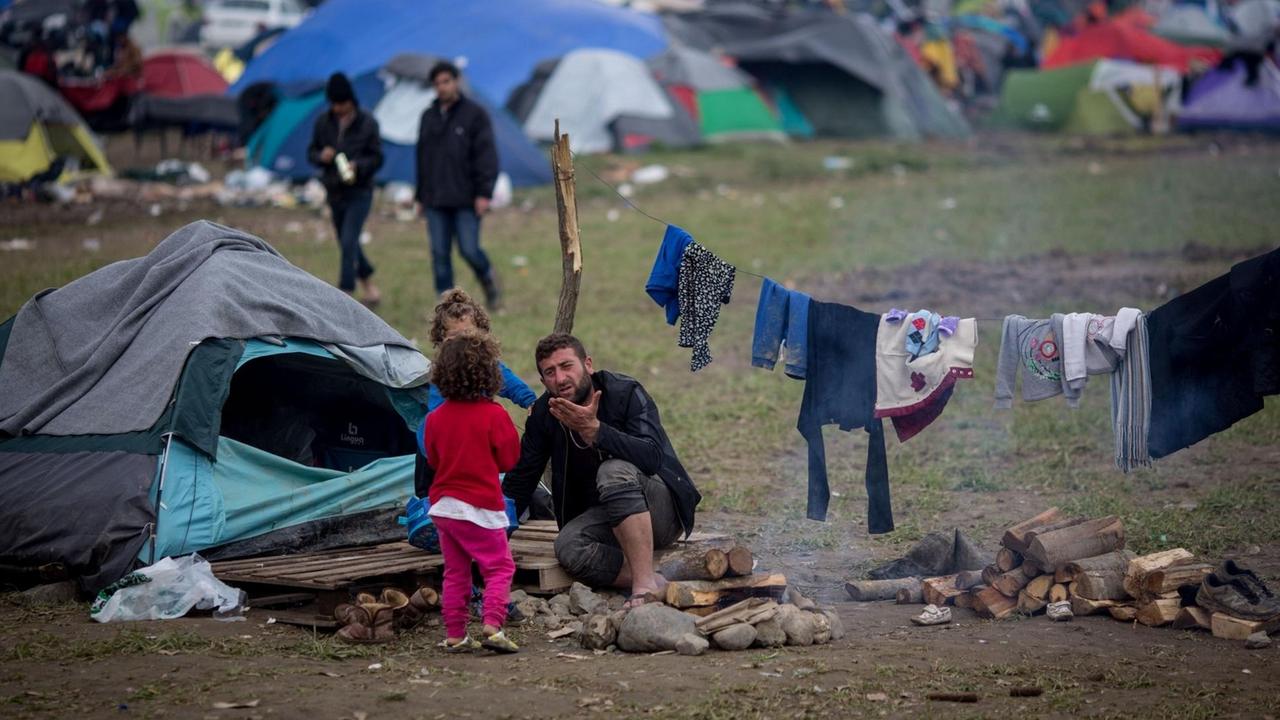 Ein Mann mit zwei Kindern sitzt am 11.03.2016 vor seinem Zelt im Flüchtlingslager in Idomeni an der Grenze zwischen Griechenland und Mazedonien.