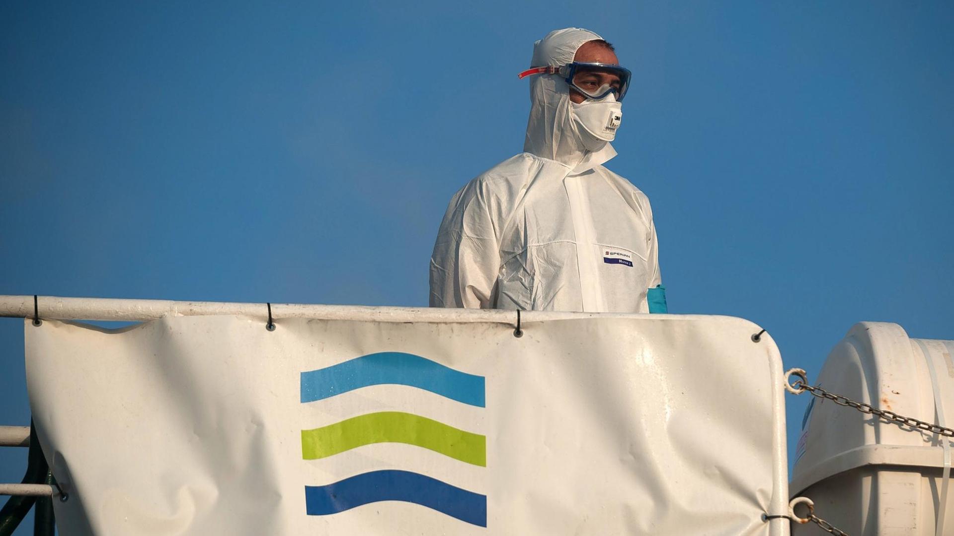Ein Mann in Schutzkleidung steht am 25. Juli 2020 vor Malaga auf einem Schiff mit Frontex-Fahne