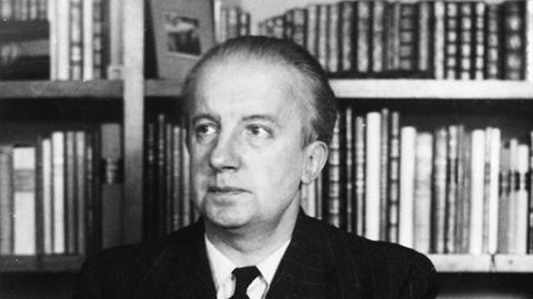 Ein Schwarz-Weiß- Foto zeigt den franzölsischen Lyriker Paul Eluard eigentllich Eugène Grindel um 1948 an einem Schreibtisch vor Bücherschrank