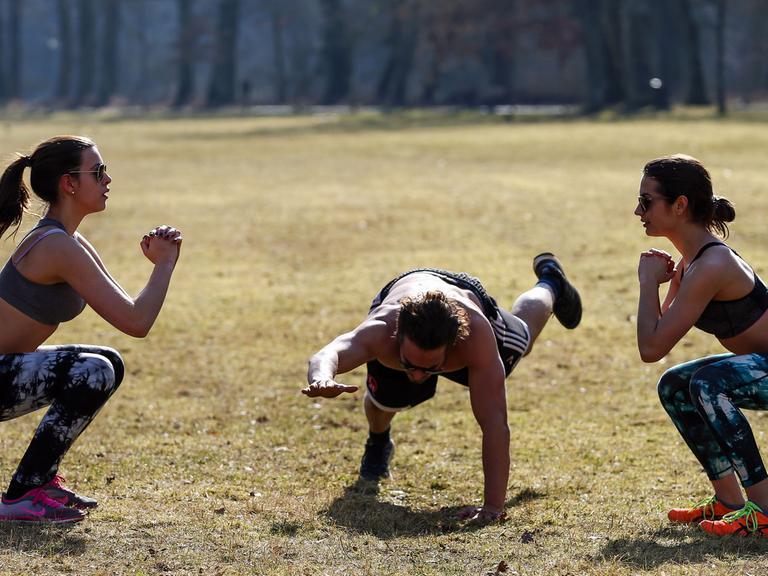 Zwei junge Frauen und ihr Trainer machen am 22.02.2015 im Stadtpark Hain in Bamberg ein Workout in der Sonne.