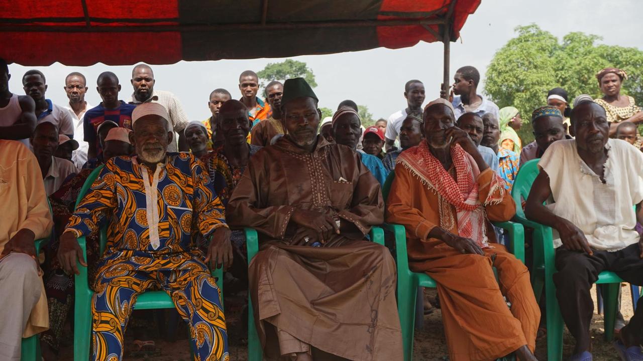 Dorfversammlung mit Männern, die bunte afrikanische Kleidung tragen.