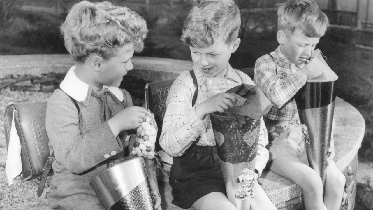 Am Tag der Einschulung ditzen drei Jungen mit Schultüten und ihren Süßigkeiten auf einer Mauer.