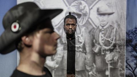 Ein weißer und ein schwarzer Mann vor einem historischen Schwarz-Weiß-Foto.