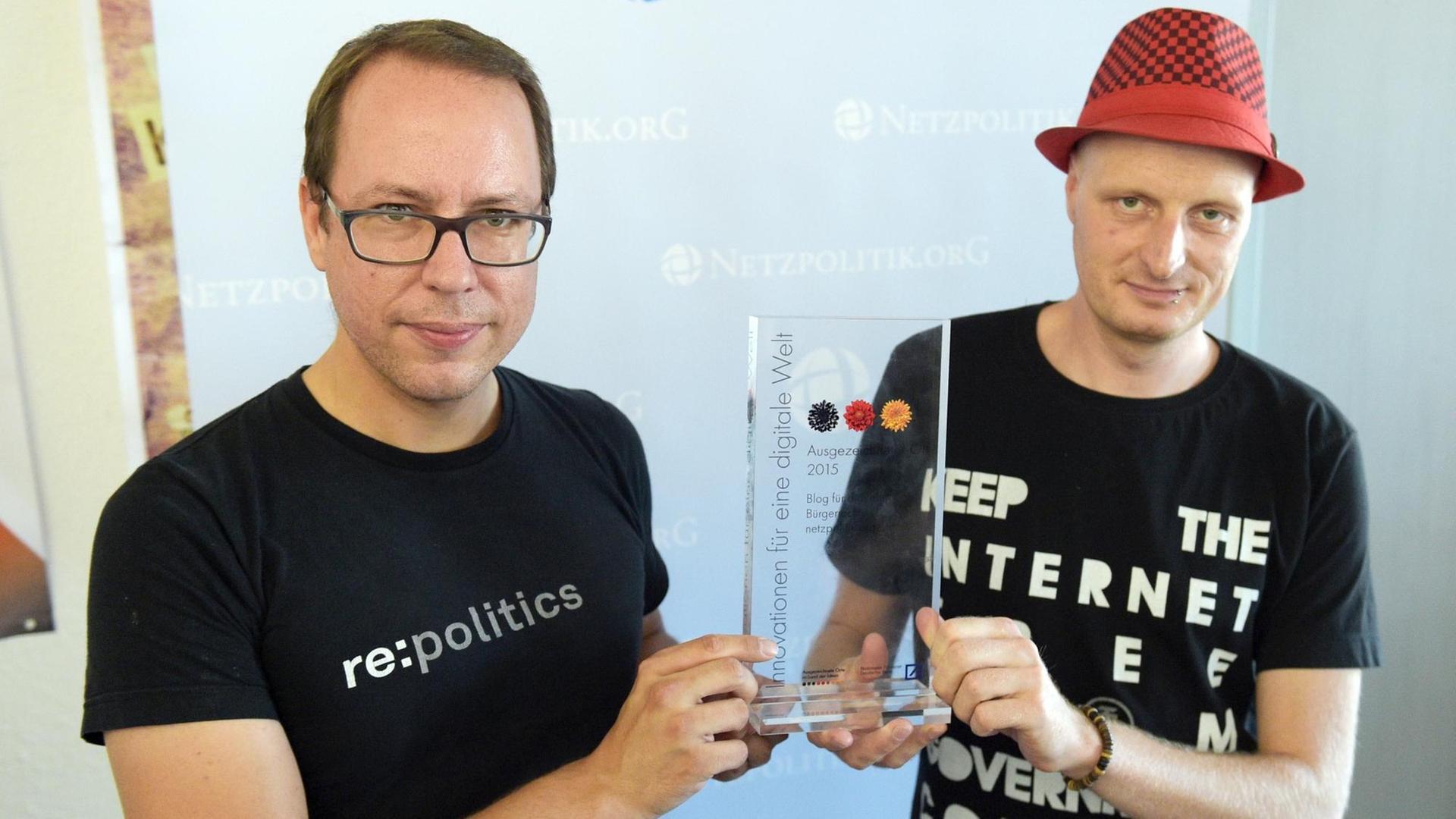 Markus Beckedahl und Andre Meister halten eine gläserne Auszeichnung zwischen sich in die Kamera
