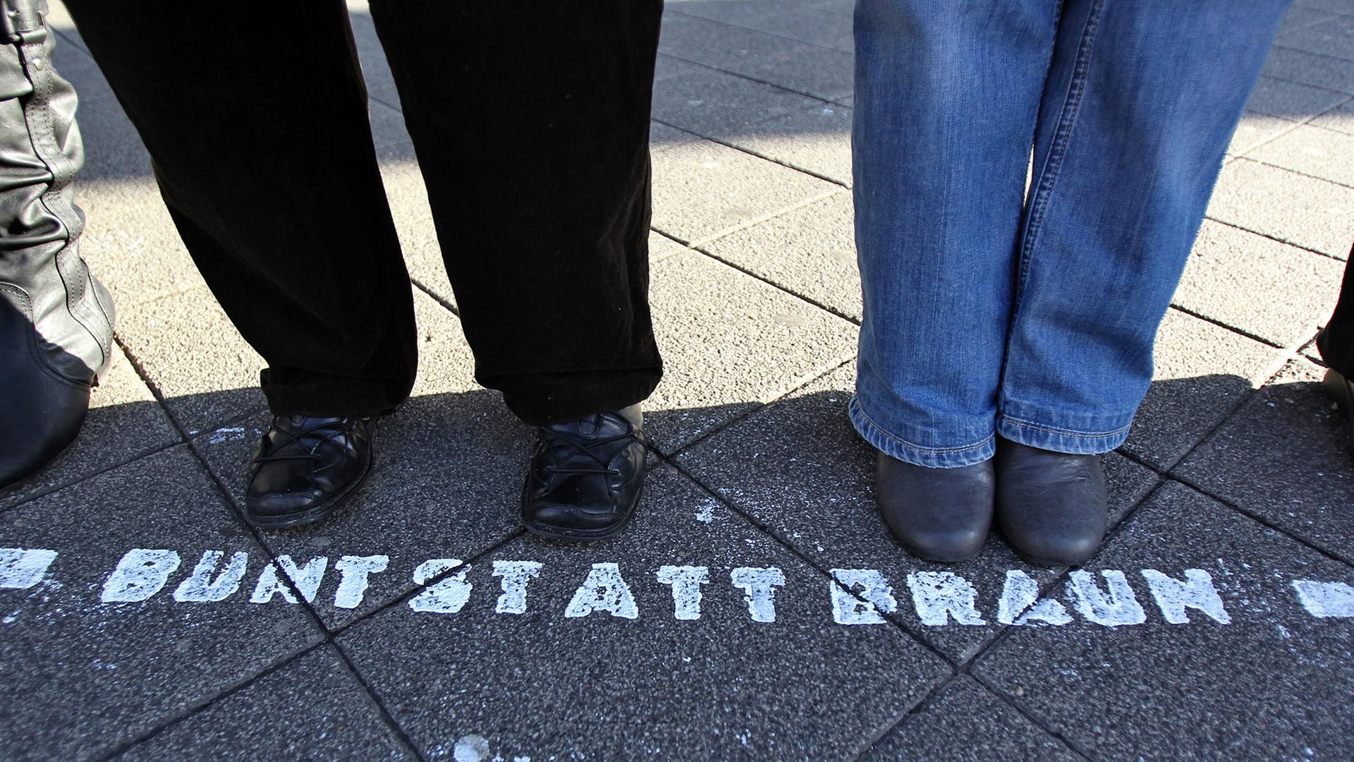 Füße einer Menschenkette bei einem Protest gegen Neonzais. Vor den Füßen steht auf der Straße "Bunt statt Braun"