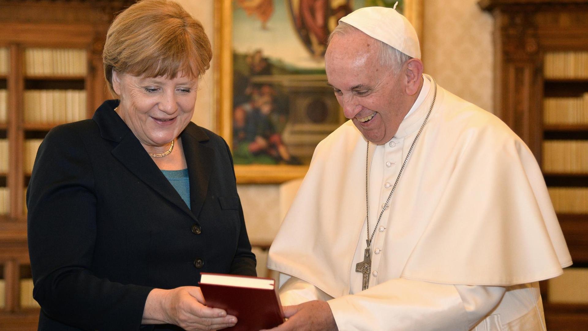 German Chancellor Angela Merkel (L) exchanges gifts with Pope Francis during a private audience on May 6, 2016 at the Vatican. Merkel is in Rome to take part in a ceremony for the awarding of Germany's famed Charlemagne Prize to Pope Francis, given to public figures in recognition of contribution to European unity. / AFP PHOTO / ALBERTO PIZZOLI