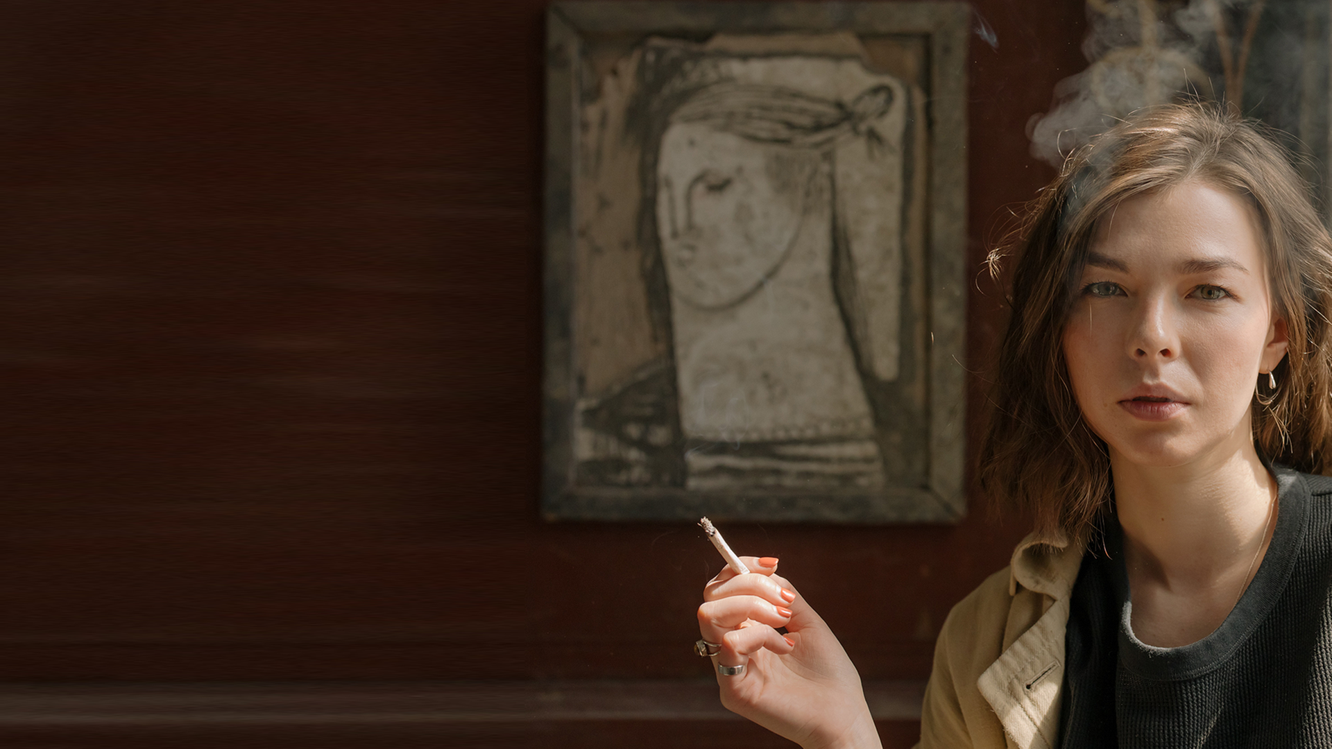 Eine junge Frau raucht vor einem gemalten Frauenporträt.