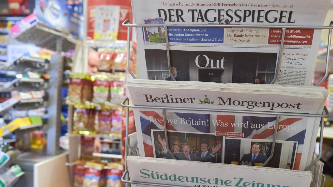 In dem Ständer klemmen der Tagesspiegel, die Berliner Morgenpopst und die Süddeutsche Zeitung. Im Hintergrund unscharf Süssigkeitenregale.