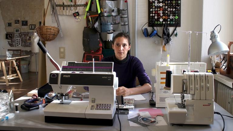 Eine junge Frau sitzt an einer Nähmaschine in ihrem Atelier 