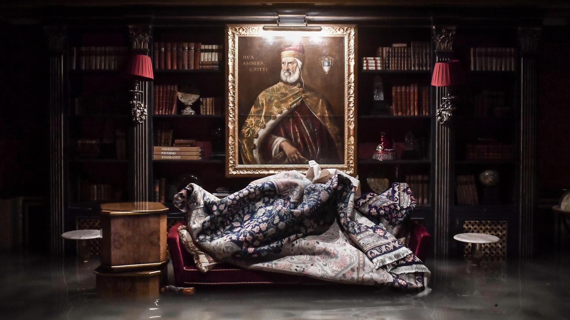 Das Foto zeigt einen Raum im überfluteten Gritti-Palast während des außergewöhnlichen Hochwasserstandes am 12. November 2019 in Venedig. An der Wand hängt ein Gemälde zwischen einer sehr alten Bücherwand. Im Vordergrund im Wasser stehend steht ein Sofa auf dem der Teppich abgelegt wurde.