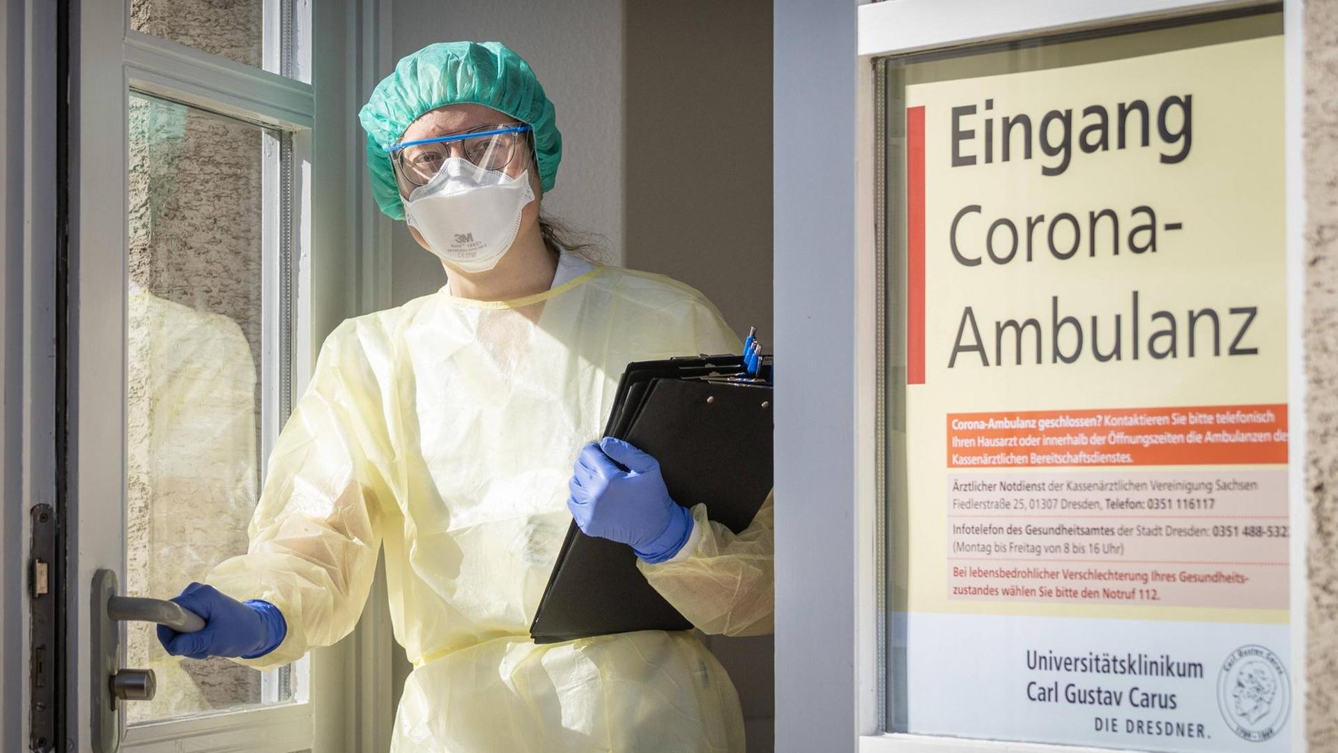 Eine Infektiologin in Schutzausrüstung steht mit vorgefertigten Fragebögen in der Eingangstür der Corona-Ambulanz an der Uniklinik Dresden.