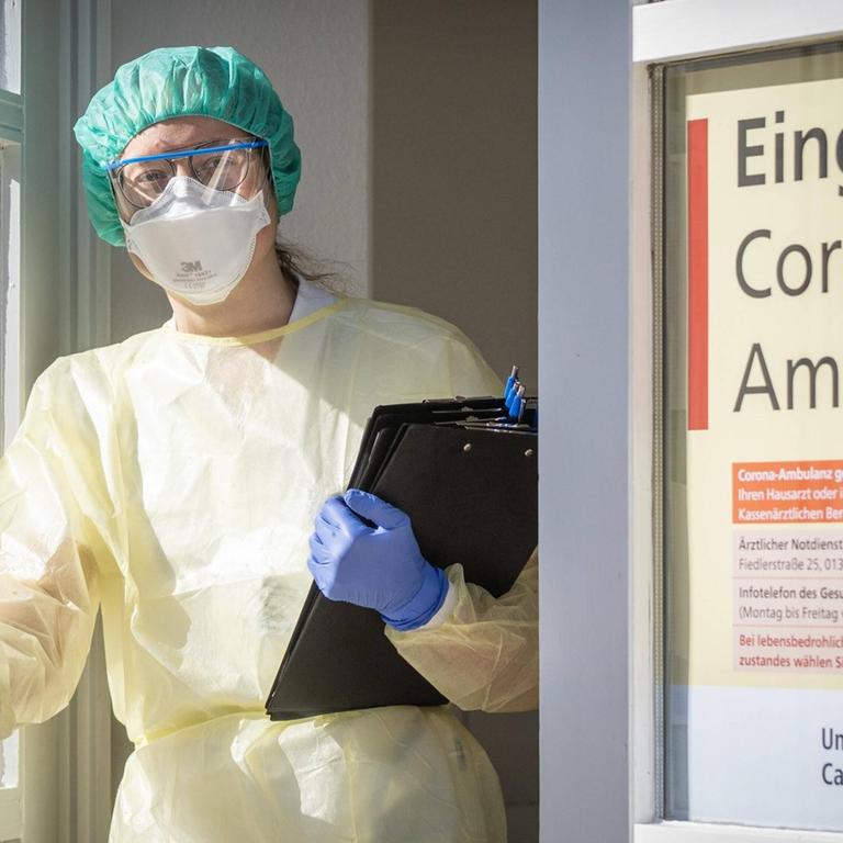 Eine Infektiologin in Schutzausrüstung steht mit vorgefertigten Fragebögen in der Eingangstür der Corona-Ambulanz an der Uniklinik Dresden.