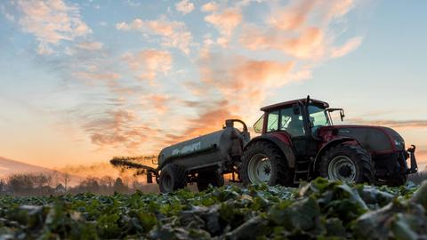 Landwirt fährt mit einem Güllefass bei Sonnenaufgang über ein angefrorenes Feld