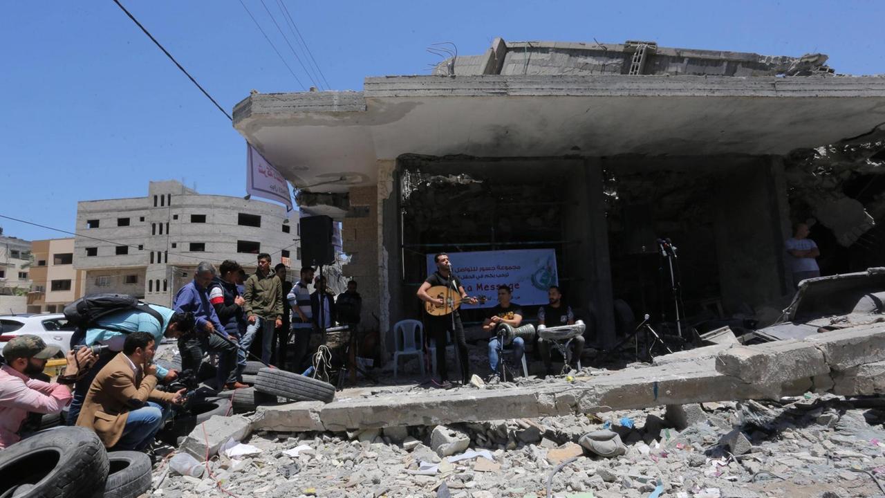 Mitglieder der Band "Dawaween" spielen am 14. Mai nach den Bombenangriffen in Gaza-Stadt vor einem zerstörten Gebäude und haben zum Boykott des ESC aufgerufen.