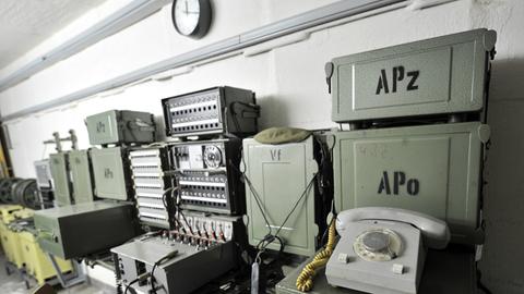 In einem Bunker sind an einer Wand ein Telefon und mehrere andere elektronische Geräte angebracht.