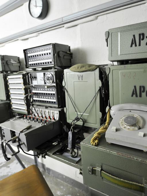 In einem Bunker sind an einer Wand ein Telefon und mehrere andere elektronische Geräte angebracht.