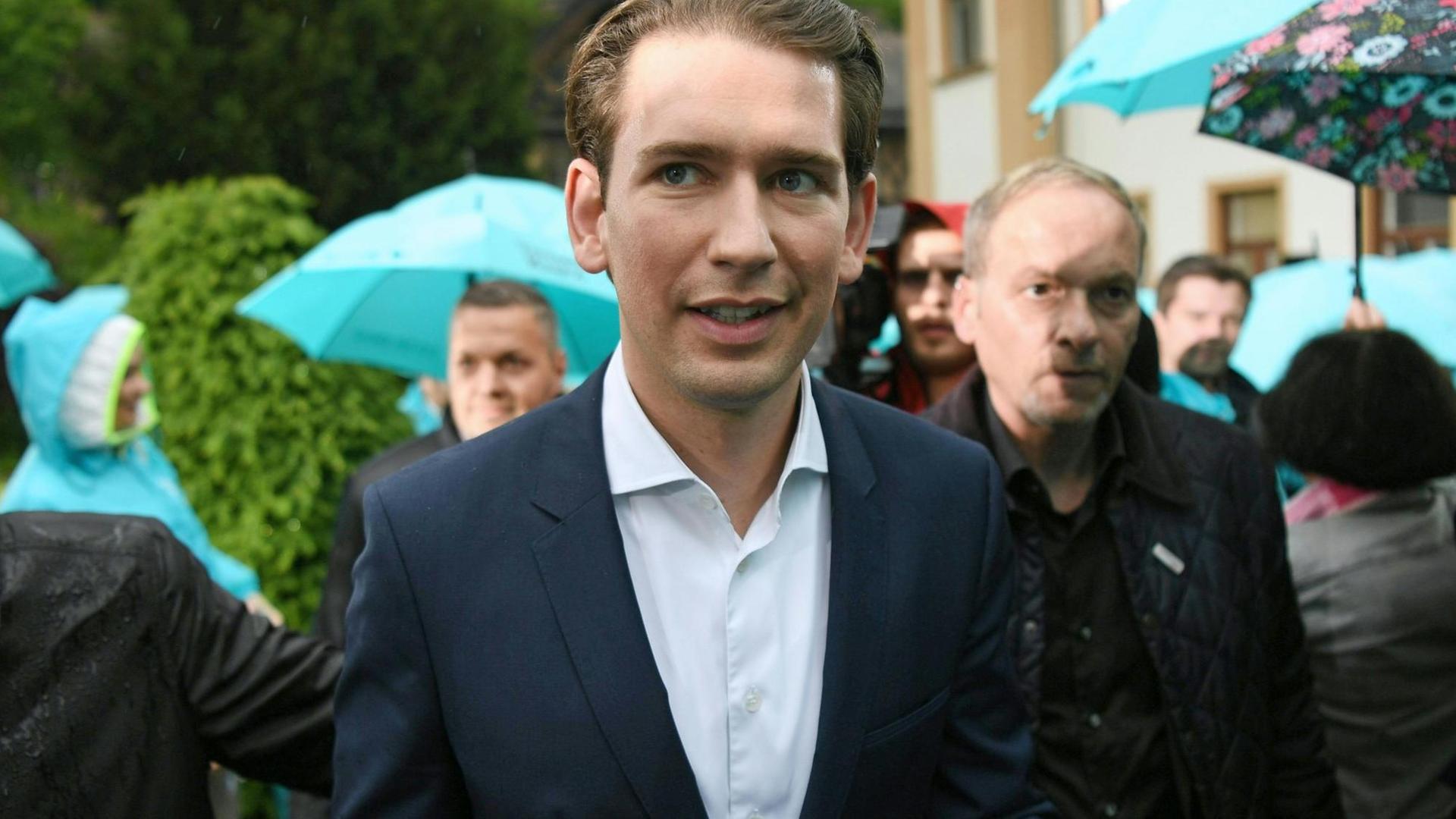 Österreichs Bundeskanzler Sebastian Kurz nach seinem Statement zum Misstrauensvotum, im Hintergrund mehrere Menschen mit türkisfarbenen Schirmen.