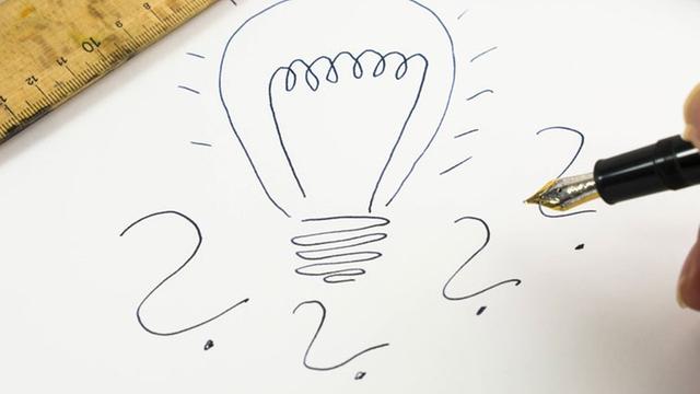 Eine gezeichnete Glühbirne mit Fragezeichen drum herum auf einem Blatt Papier, eingerahmt von einem Lineal und einer Lupe