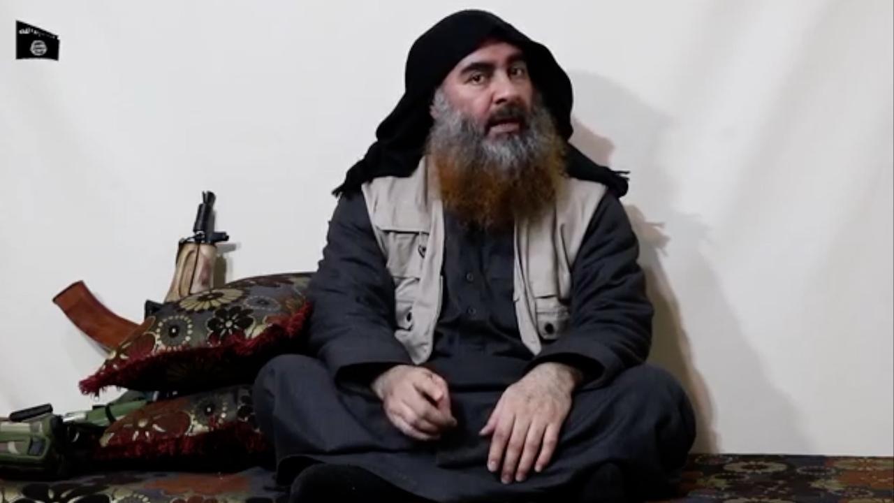 Al-Bagdadi sitzt auf dem Boden und spricht, hinter ihm lehnt eine Waffe an der Wand.