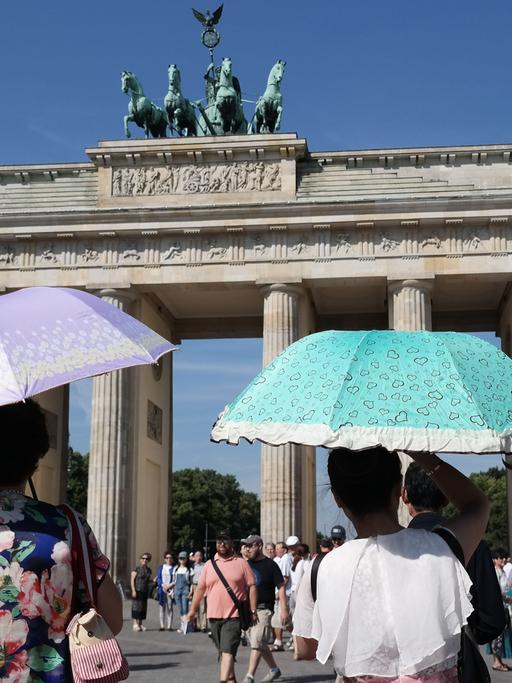 Touristen schützen sich mit Schirmen vor den Sonnenstrahlen vor dem Brandenburger Tor in Berlin.