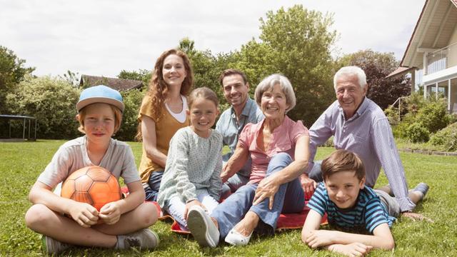 Eine Familie sitzt auf dem Rasen. Kinder, Eltern und Großeltern lächeln.