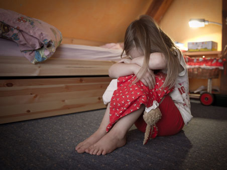 Ein kleines Mädchen sitzt weinend auf dem Fußboden in ihrem Zimmer.