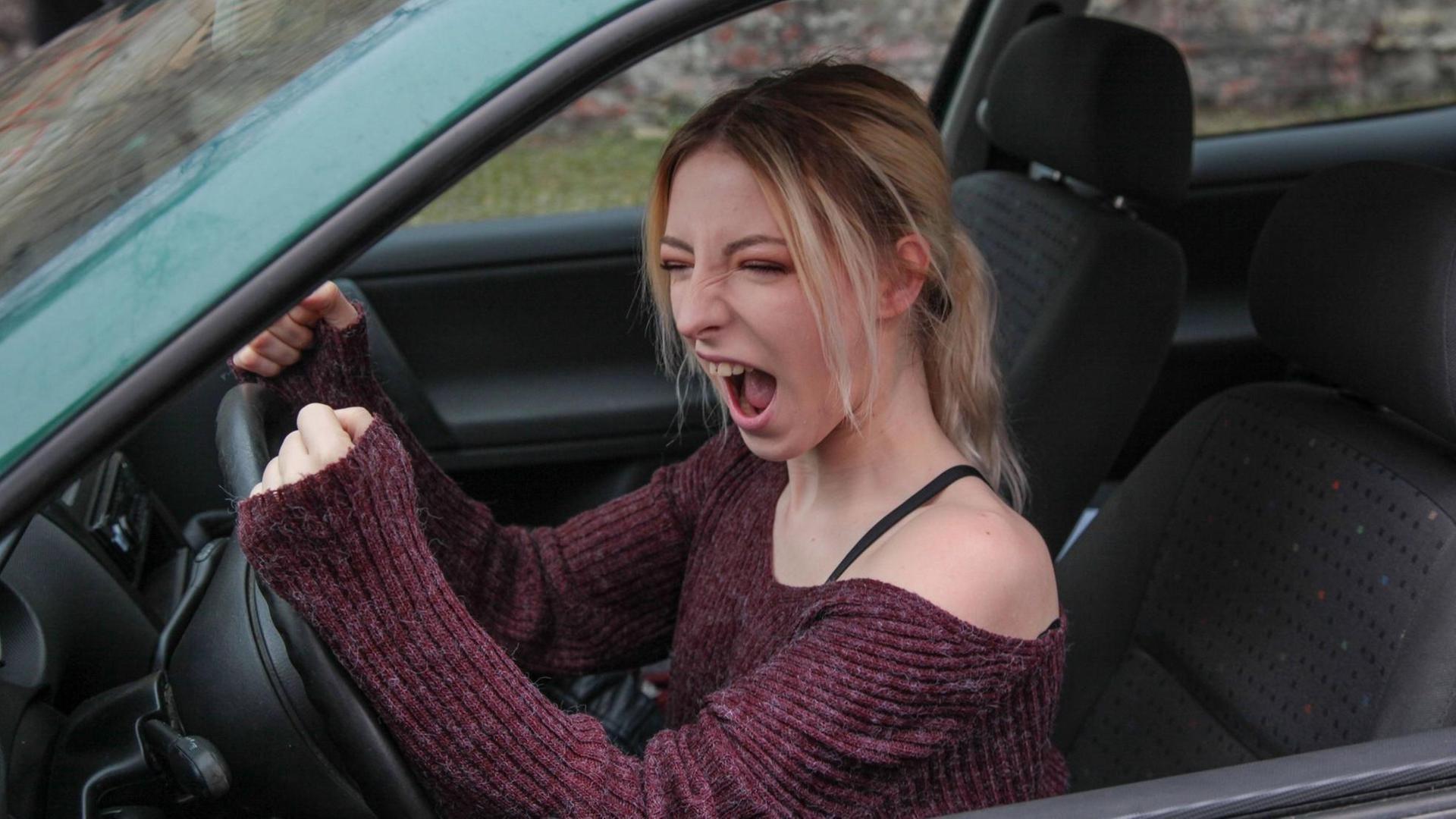 Eine junge Frau schimpft hinterm Autosteuer.