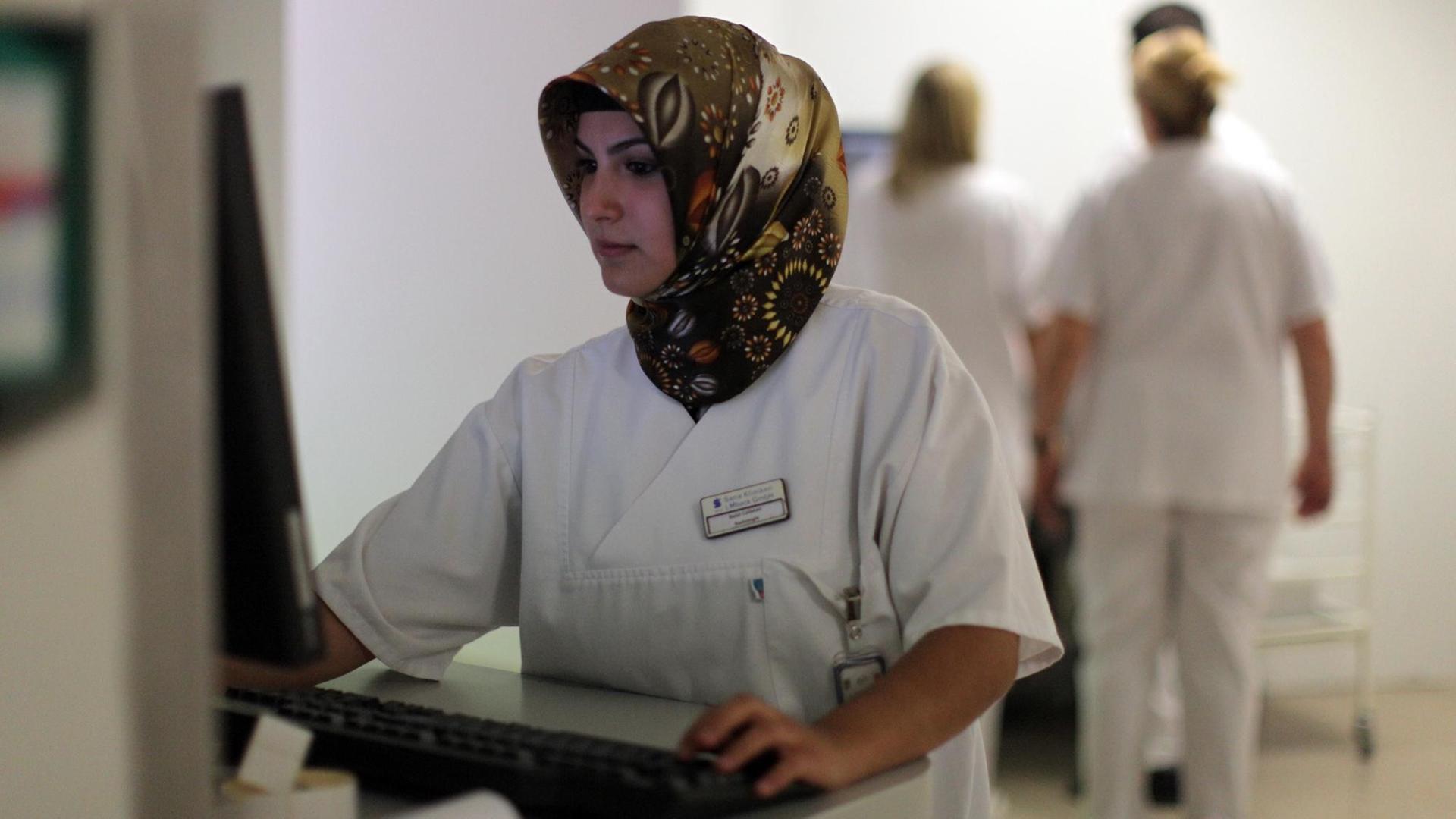 Eine Medizinisch-technische Assistentin mit Kopftuch arbeitet an einem Computer.