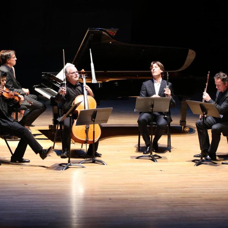 Fünf Musiker sitzen mit ihren Instrumenten auf einer ins Scheinwerferlicht getauchten Bühne.