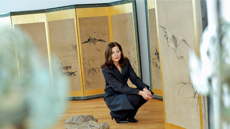 Die Schriftstellerin Ursula Krechel hockt gedankenversunken in einer Ausstellung. Auf Stellwänden sind Zeichnungen von Vögeln und Gräsern zu sehen. Die Schriftstellerin Ursula Krechel hockt gedankenversunken in einer Ausstellung. Auf Stellwänden sind Zeichnungen von Vögeln und Gräsern zu sehen.