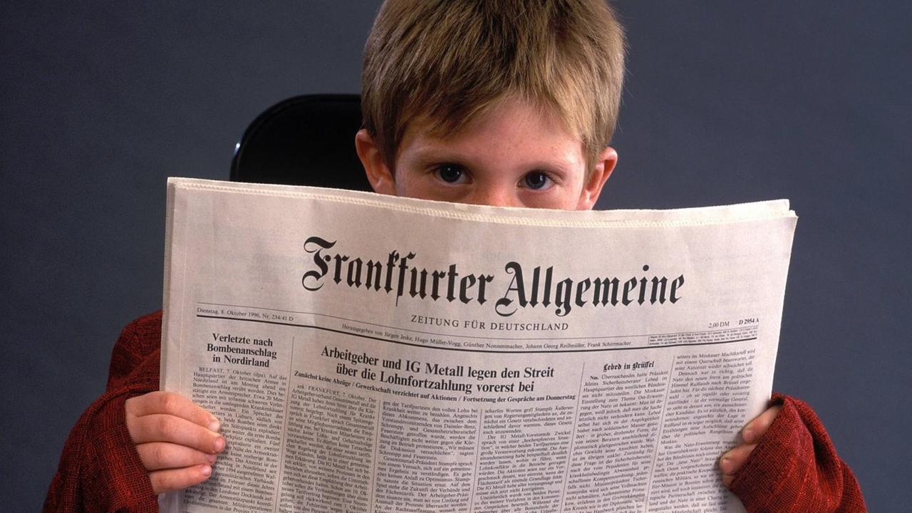 Ein Junge blickt hinter eine Ausgabe der FAZ hervor.