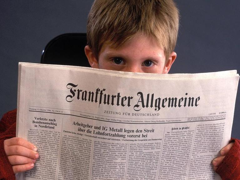 Ein Junge blickt hinter eine Ausgabe der FAZ hervor.