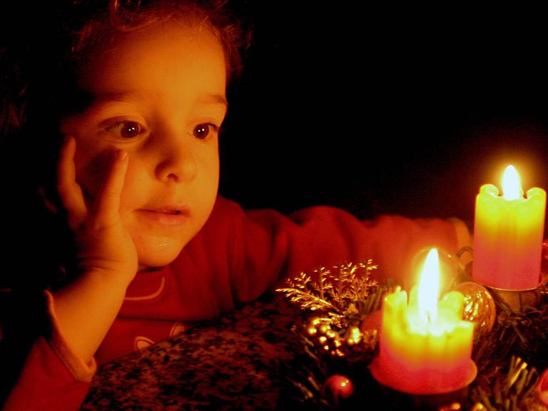 Ein Kind betrachtet brennende Kerzen auf einem Adventskranz.