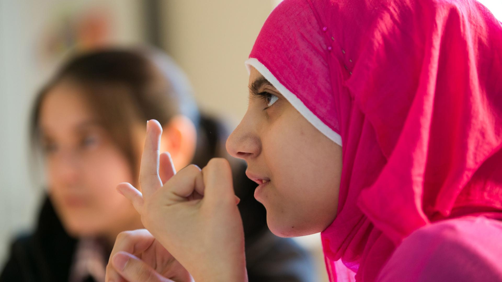 Ein syrisches Flüchtlingsmädchen während des Schulunterrichts mit rosafarbenen Kopftuch.
