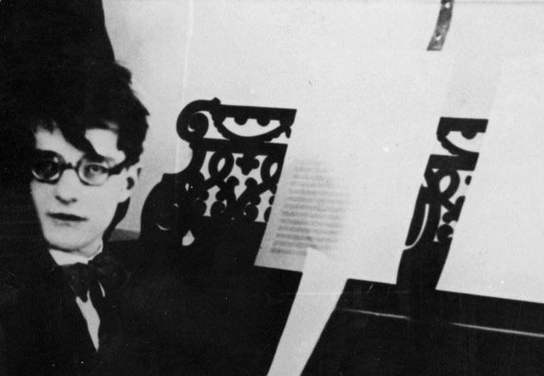 Ein junger Mann mit auffällig schwarz gerandeter Brille sitzt seitlich an einem Flügel.