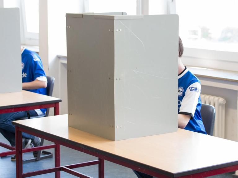 Zwei Wähler gekleidet in ein Fußballtrikot sitzen in einem Wahllokal in einer Wahlkabine