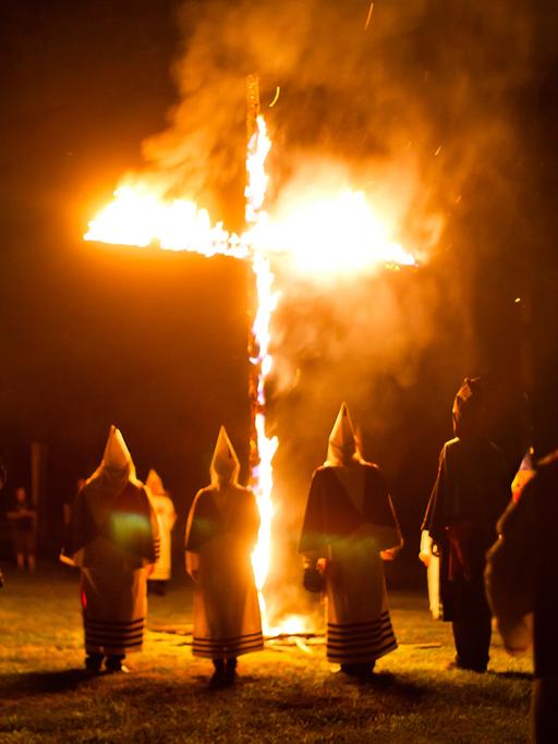 Mitglieder des Geheimbundes Ku-Klux-Klan in den USA stehen in weißen Gewändern und Kapuzen um ein brennendes Kreuz.