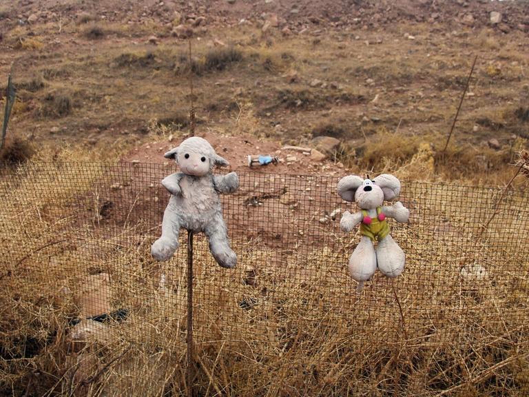Zwei Kuscheltiere hängen an einem Zaun vor einem Massengrab nahe des Sindschar-Gebirges im Irak. Dort wurden Massengräber worden. Hier tötete die Terrormiliz IS massenhaft Jesiden.
