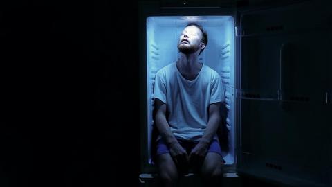 Ein Mann sitzt im offenen Kühlschrank.