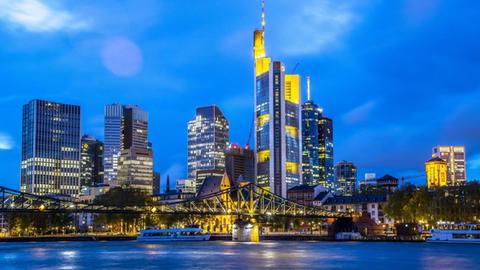 Die erleuchtete Skyline der Innenstadt von Frankfurt am Main bei Nacht, im Vordergrund der Main