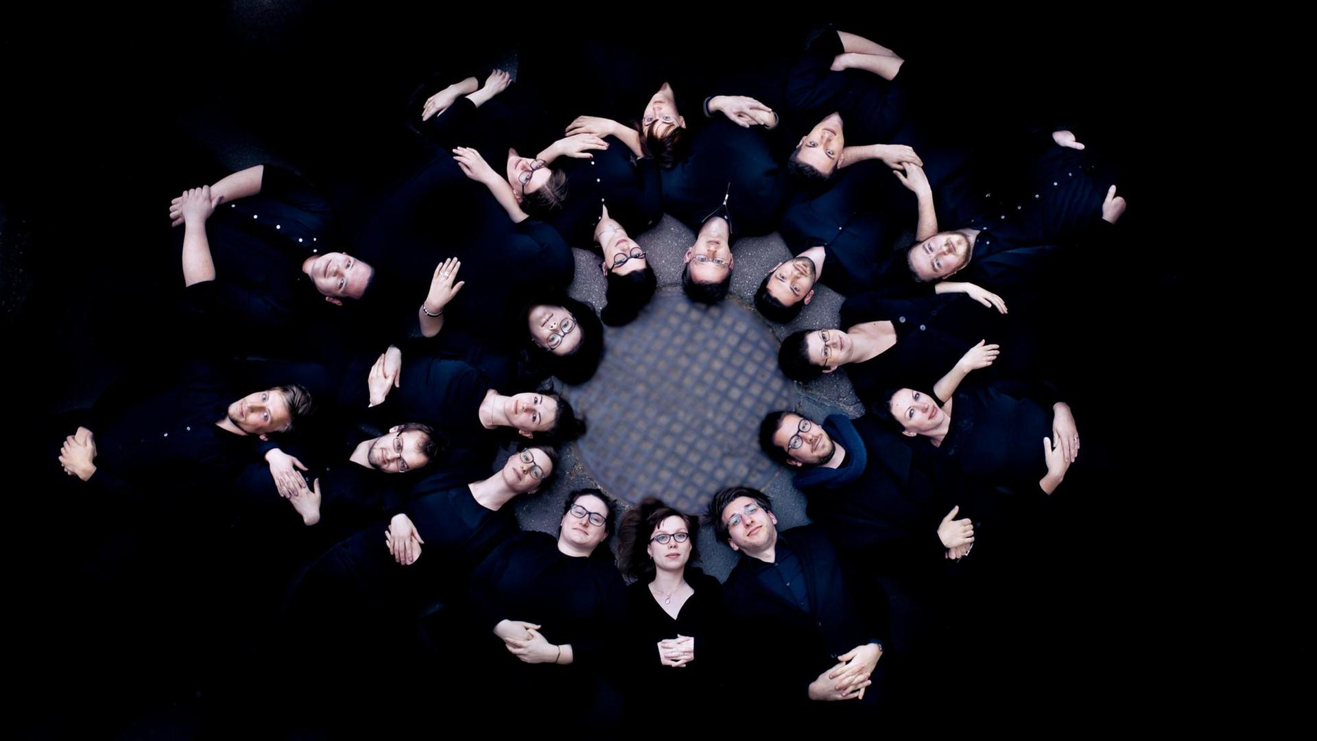 Gruppenbild der Sänger liegend vor schwarzem Hintergrund