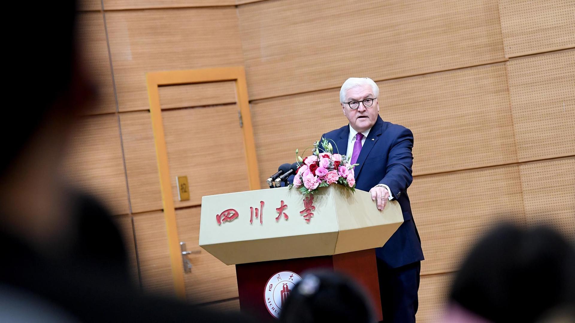 Frank-Walter Steinmeier hält sich an einem Rednerpult fest, auf dem chinesische Schriftzeichen stehen.