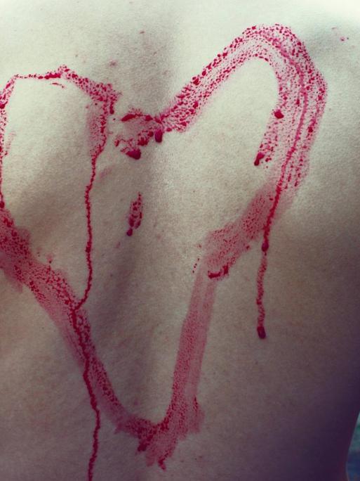 Eine rotes gemaltes Herz auf einem Männerrücken mit Gänsehaut, die Farbe läuft herunter.