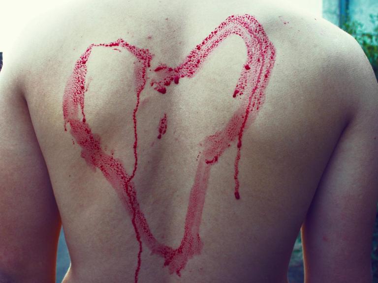 Eine rotes gemaltes Herz auf einem Männerrücken mit Gänsehaut, die Farbe läuft herunter.