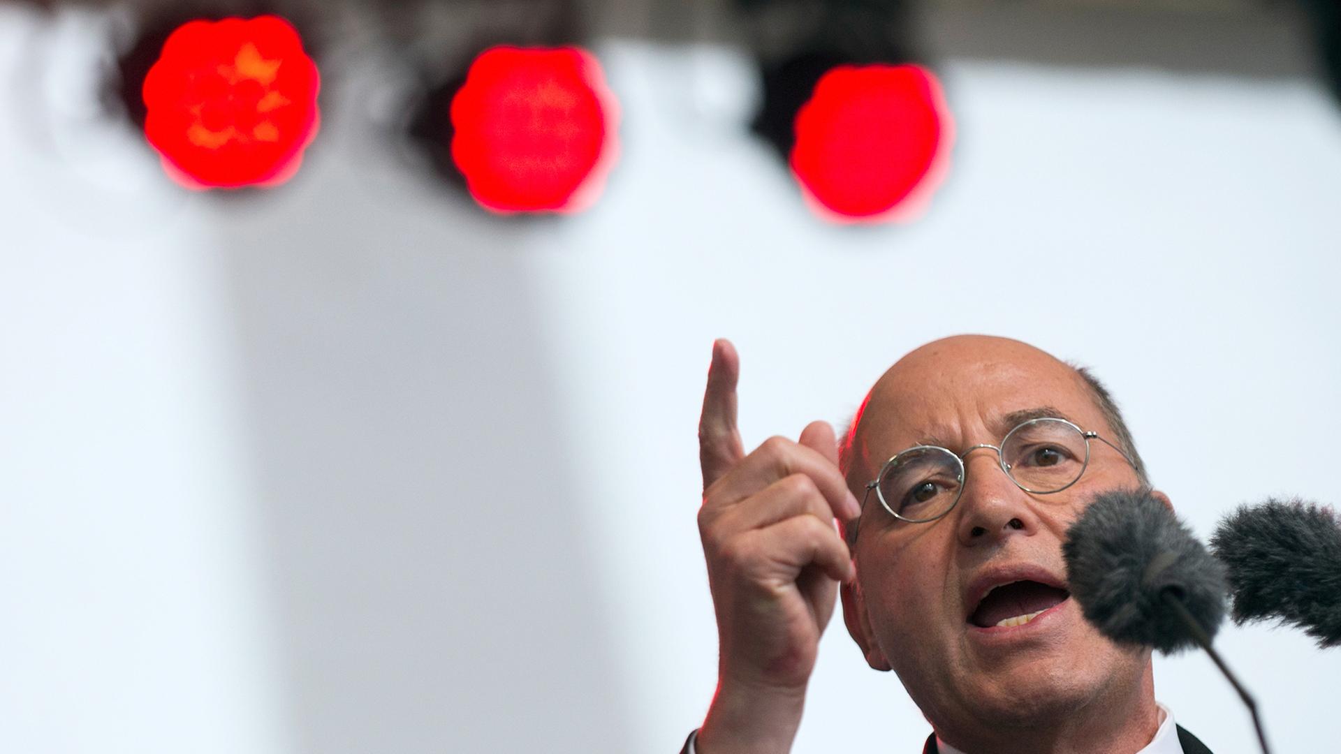 Gregor Gysi spricht am 20. September 2013 in Berlin vor einem Mikrofon, vor weißem Hintergrund. Oben im Hintergrund sind drei rote Scheinwerfer zu sehen.