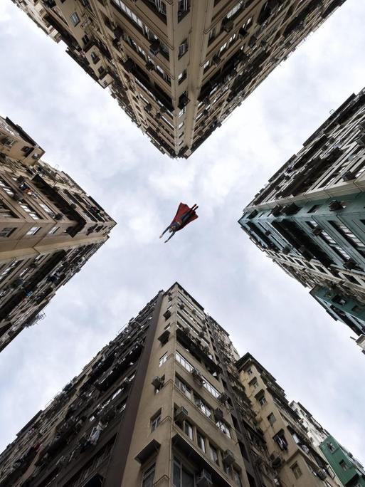 Aus der Froschperspektive sieht man Superman zwischen Häuserschluchten hindurch fliegen.