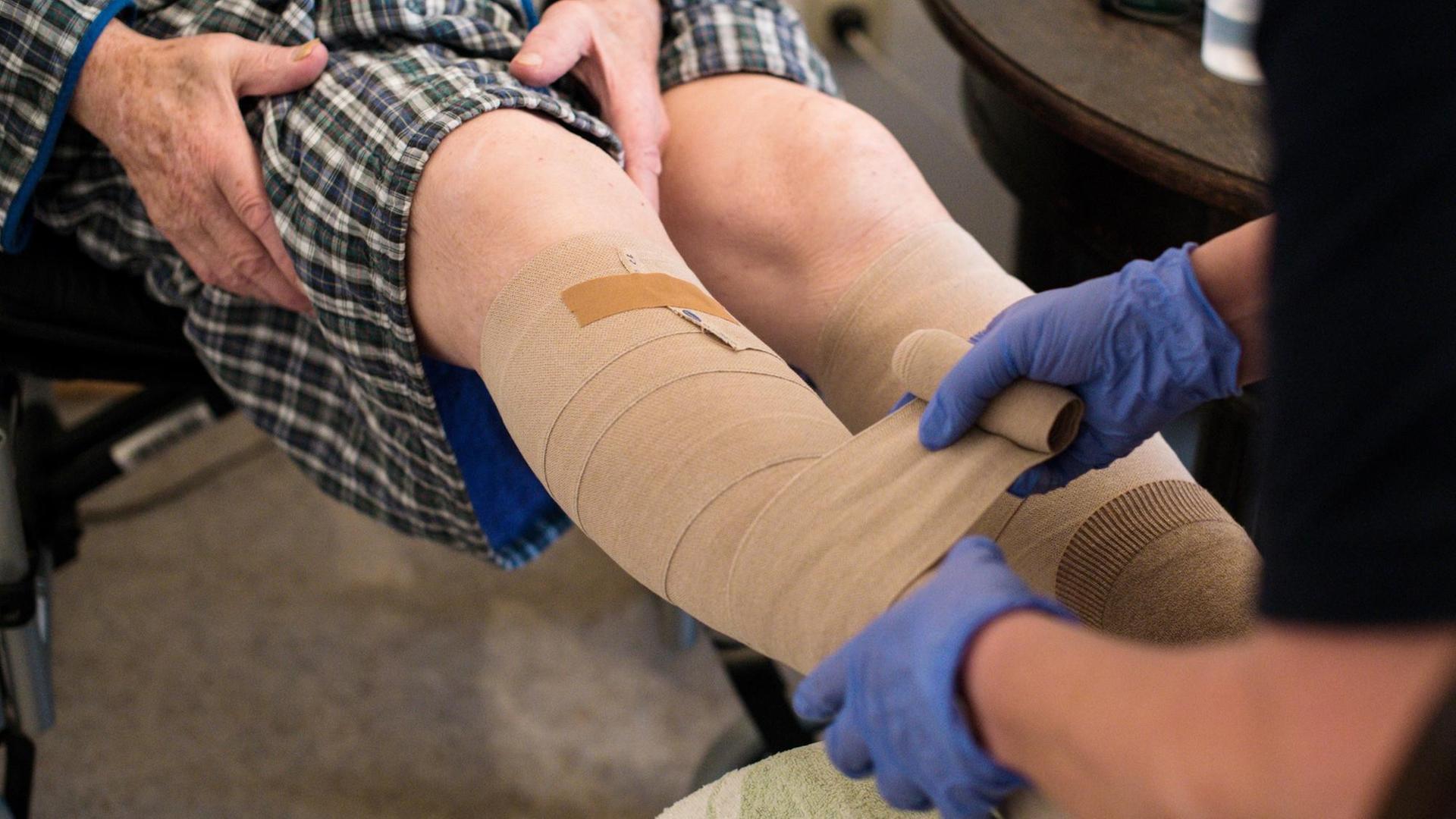 Eine ambulante Pflegerin bandagiert die Beine eines alten Mannes. Foto: Jana Bauch/dpa | Verwendung weltweit