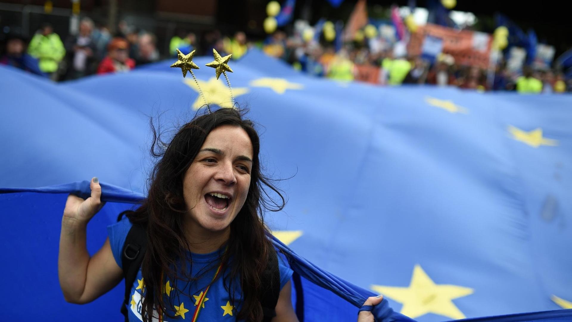 Eine junge Frau hält eine riesige EU-Fahne fest. Eine junge Frau hält eine riesige EU-Fahne fest.