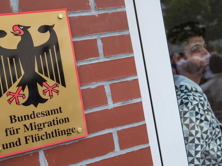 Schild des Bundesamts für Flüchtlinge und Migration, Asylbewerber hinter einer Glasscherbe