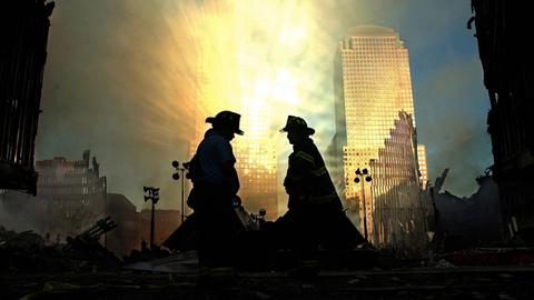 Vor reflektierenden Lichtstrahlen setzen sich die Silhouetten zweier Feuerwehrmänner ab, die die Zerstörung am Ground Zero begutachten.